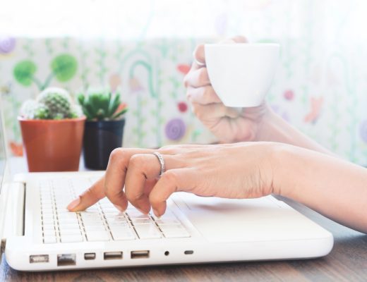 Asmuo rašo SEO optimizuotą straipsnį nešiojamame kompiuteryje, šalia užrašai ir kavos puodelis.