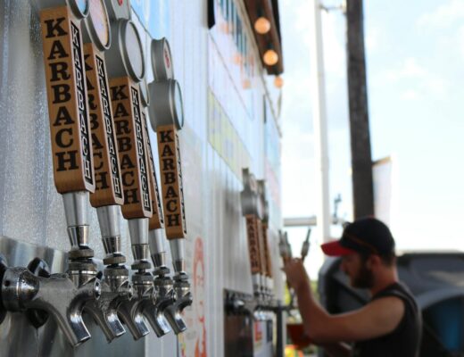 Mobilus baras šventėje lauke, profesionalūs barmenai ruošia kokteilius, svečiai mėgaujasi šventine atmosfera.