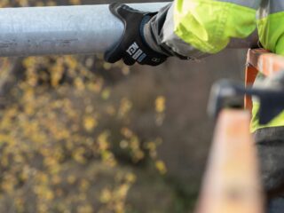 Specialistas kruopščiai tikrina apsauginių apraišų siūles ir tvirtinimo elementus prieš darbą aukštyje.